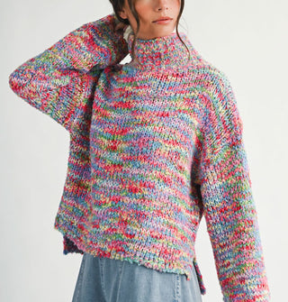 Model with one arm upraised wears a multicolored, oversized  turtleneck sweater