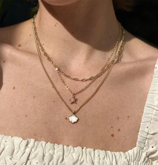 Model wears a dainty mother of pearl and gold seashell chain necklace with other gold chain necklaces