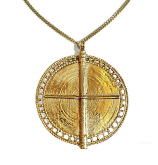 Large round gold-toned medallion with lacy edge and central "t" or cross formed by two perpendicular ridges is attached to a thin curb chain