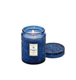 Lit single-wick Mediterranean Lemon scent Voluspa candle in an embossed blue glass vessel with matching lid removed and set to the side