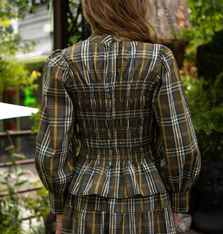 Model with back to the camera wears a plaid smocked blouse with mock neckline, peplum hem, and balloon sleeves gathered in a wide cuff paired with a matching skirt