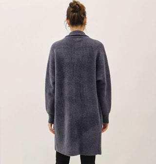 Model facing away from the camera wears a long, dark muted blue fuzzy coat/cardigan with collar