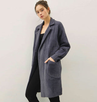 Model wears a long, dark muted blue fuzzy coat/cardigan with notched collar and pocket