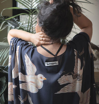 Model facing away from the camera wears a black robe with print of large white doves