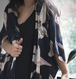 Model wears a loose-fitting, silky black robe with print of large white doves carrying banners in their beaks