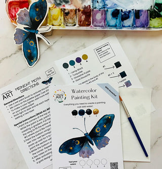 Components of a "Midnight Moth" Watercolor Painting Kit on a marble tabletop with paint palette