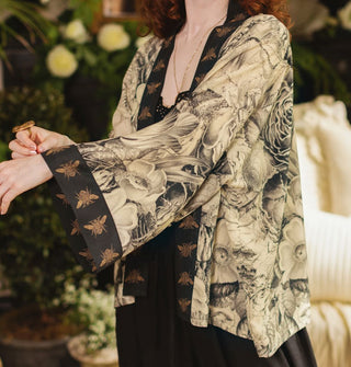 Model with arms extended forward wears a cropped kimono-style cardigan with black and white floral print and contrasting bee print borders