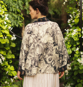Model facing away from the camera wears a cropped kimono-style cardigan with black and white floral print and contrasting bee print borders