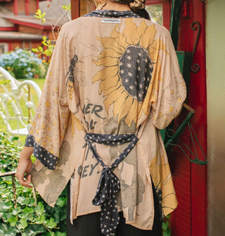 Model facing away from the camera wears a kimono-style cardigan with sunflower motif complemented by black and white star print borders, belt and accents