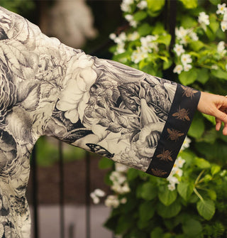 Model's outstretched arm shows detail of the wide sleeve of a top that features a black and white floral print with contrasting bee print cuff