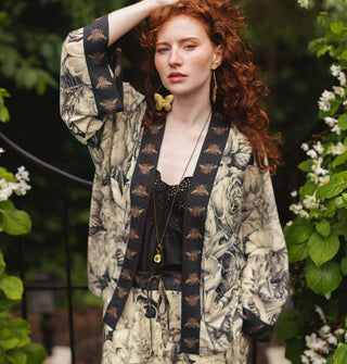Model with one hand upraised wears a cropped kimono-style cardigan with black and white floral print and contrasting bee print borders