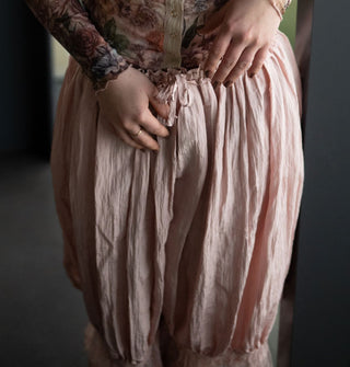 Model wears light pink pantaloons with lace trim and a ruffled tie waist