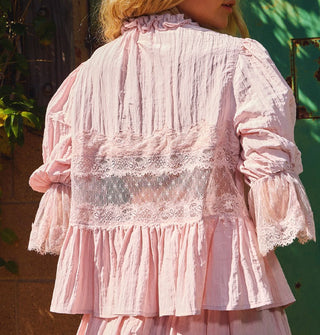 Model wears a lace-trimmed pink blouse with puffy, elasticated sleeves and a ruffled collar