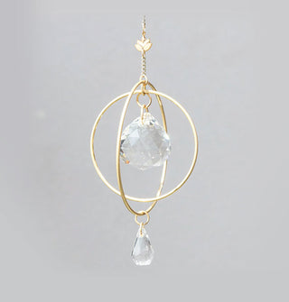 Gold-toned ornament with double rings and a lotus charm hang from a gold chain with a teardrop-shaped crystal in the center and a smaller teardrop-shaped crystal at the base