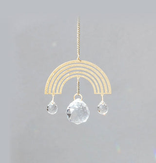 Gold-toned rainbow-shaped charm hangs from a gold chain with two small and one larger teardrop-shaped crystals hanging from its center and sides