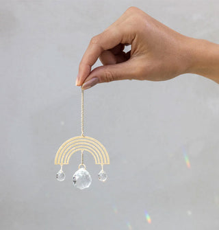 Model's hand holds a gold and crystal rainbow suncatcher ornament by its hanging chain