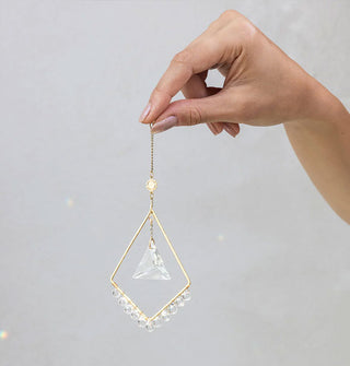 Model's hand holds the Mini Sun Diamond gold and crystal suncatcher by its chain extension