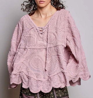 Model wears a dusty pink, oversized-fit, scalloped-edge crocheted blouse with paisley pattern and lace-up neckline