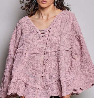 Model wears a dusty pink, oversized-fit, scalloped-edge crocheted blouse with paisley pattern and lace-up neckline