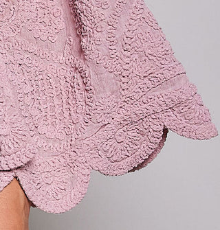 Closeup of a scalloped-edge sleeve hem on a heavily crocheted pink blouse