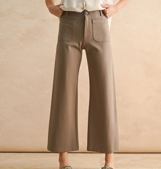 Model wears a pair of cropped flared tan pants with pockets, belt loops, and button closure