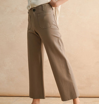 Model wears a pair of cropped flared tan pants with pockets, belt loops, and button closure