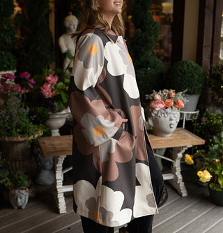 Smiling model wears an overcoat with large floral print in a brown, gray, black, and yellow color palette