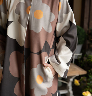 Model poses with hand in the pocket of an overcoat with large floral print in a brown, gray, black, and yellow color palette