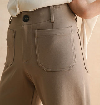 Model wears a pair of tan pants with pockets, belt loops, and button closure