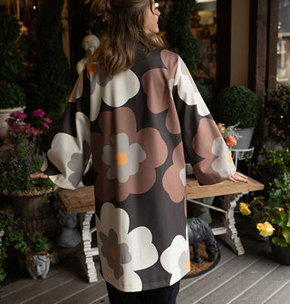 Model wears an overcoat with large floral print in a brown, gray, black, and yellow color palette
