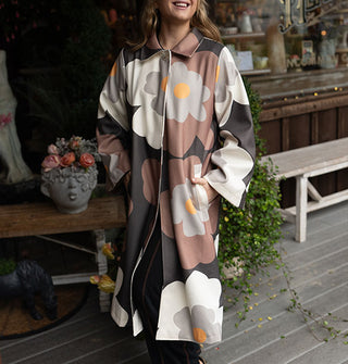 Smiling model wears an overcoat with large floral print in a brown, gray, black, and yellow color palette