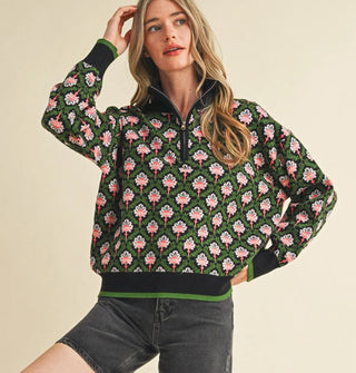 Model wears a green, black, and pink floral print pullover with half zipper, mock neckline, and knit hem and cuff bands