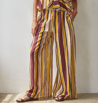 Model wears wide-legged brown, burgundy, rose, gold, and white striped pants paired with a matching top