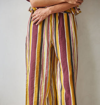 Model with arms crossed wears wide-legged brown, burgundy, rose, gold, and white striped pants