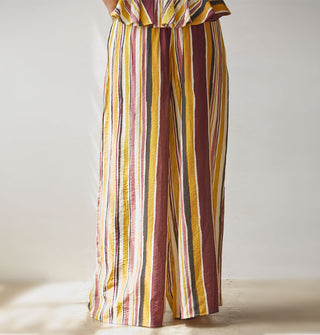 Model facing away from the camera wears wide-legged brown, burgundy, rose, gold, and white striped pants paired with a matching top