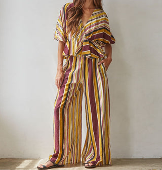 Model wears a brown, burgundy, rose, gold, and white striped loose-fitting top and pants set