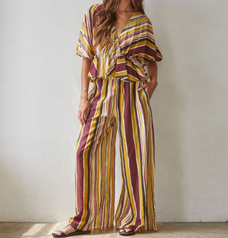 Model wears a brown, burgundy, rose, gold, and white striped loose-fitting top and pants set