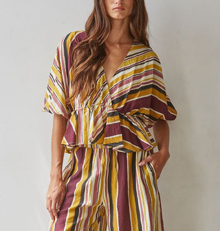 Model wears a brown, burgundy, rose, gold, and white striped V-neck top with gathered waist and puff elbow-length sleeves paired with matching pants