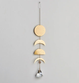 Gold toned brass circle, crescent, and semicircle charms hang from a chain with a small moonstone and conical crystal at the bottom