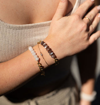 Close-up of a model's arm wearing moonstone and chocolate moonstone bead bracelets, each on a chunky brass curb chain