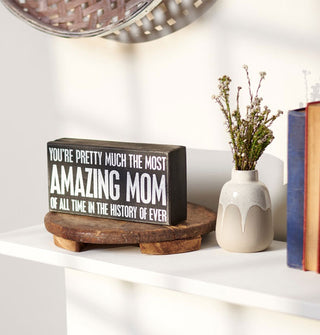 You're Pretty Much the Most Amazing Mom black and white box sign is staged on a rustic wooden pedestal next to a flower vase and stack of books