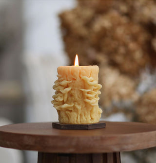 Lit beeswax candle that resembles oyster mushrooms growing on a tree trunk