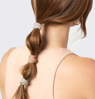 Model wears three light-colored nylon hair elastics in a low bubble ponytail