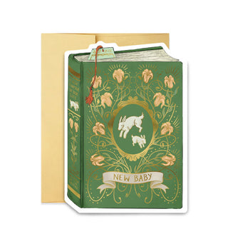 Green greeting card in front of a gold envelope is designed to resemble a book with jumping white rabbits on its over inside an ornate gold floral frame above the words, "New Baby" in a banner; on its spine is the message, "A new chapter in your life written by the universe"