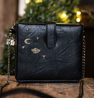 Back of black handbag with chain strap features several beaded stars, Saturn, and a crescent moon