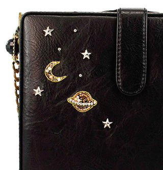 Closeup of beaded crescent moon, Saturn, and stud stars on a black handbag with chain strap and flap closure