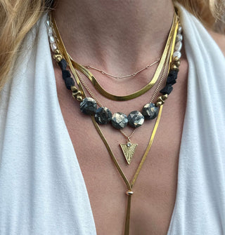 Model wears a shimmery stone necklace with several other gold necklaces