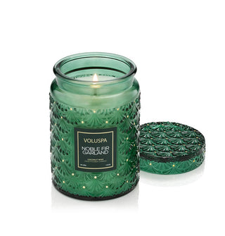 Lit Noble Fir Garland Voluspa candle in embossed green glass vessel with matching lit set to one side