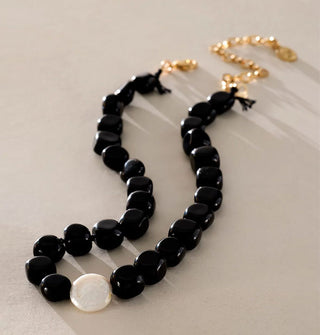 Necklace with gold clasp and extender chain is strung with polished black obsidian stones and one white accent pearl