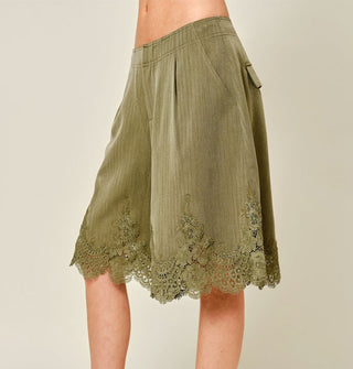 Model wears wide-legged olive green shorts with lace hem detail